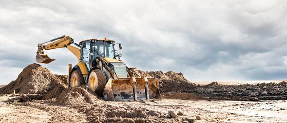 A universal excavator loader moves sand at a construction site. Excavation work at a construction site for a future project © Anoo