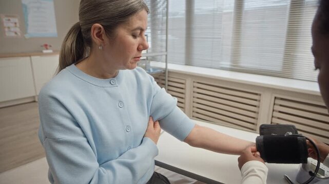 Black female healthcare professional measuring blood pressure of Caucasian female patient using digital cuff during routine checkup in modern clinic