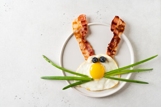Easter concept with funny fried egg bunny and becon on plate on whitebackground, top view