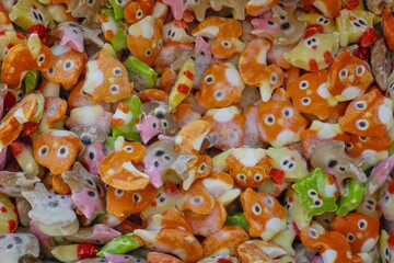 A vibrant, close-up photograph showcasing a multitude of Japanese arare rice crackers in various whimsical animal shapes and vivid colors, creating a textured food background.