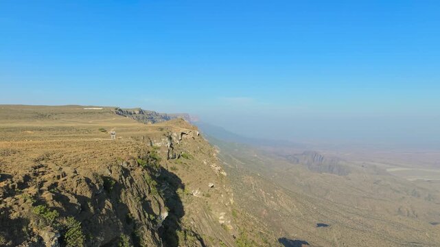 Aerial view of steep rocky cliffs and a high plateau overlooking the deep valley floor and mountain ridges at Jabal Samhan, Salalah, Oman.