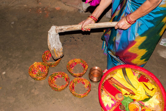woman&rsquo;s hands collecting sacred soil from the ground using a traditional kudal (spade) and placing it into five small decorative tokri baskets during the Matkor ceremony of an Indian bihari wedding.