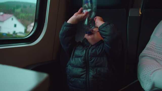 Toddler sitting on train seat trying to drink last drops from empty water bottle expressing persistence curiosity and everyday family travel moment