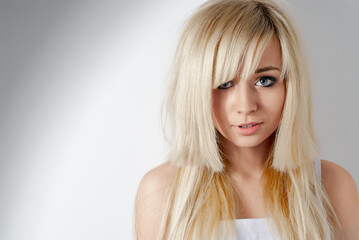Naklejka premium Stylish blonde-haired young woman gazing confidently into the camera against a minimal background, showcasing elegance and modern style, perfect for fashion, lifestyle, or beauty concepts.