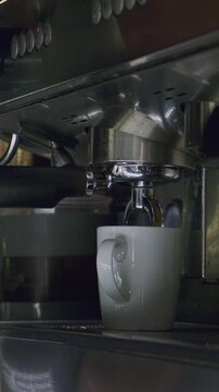 Fresh espresso flowing from professional coffee machine into white ceramic cup. Coffee preparation process, barista workflow, specialty beverage service