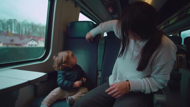 Toddler stretched across train seat playing with toy as motion passes outside while mother looks on conveying energy movement patience and lived in family travel moment