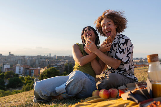 Happy young couple enjoying picnic eating pastries laughing outdoor