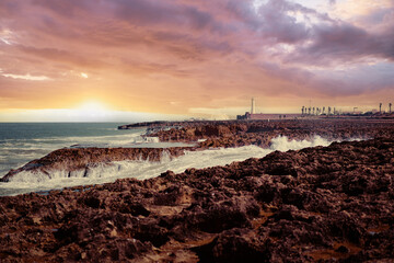 Stunning coastline during sunset featuring dramatic clouds, lighthouse, and ocean waves crashing against the rocky shores. Vibrant scenery radiates tranquility and the enduring allure of nature.