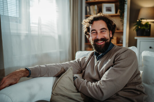 Smiling bearded man relaxing on sofa feeling happy at home