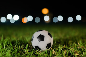 Naklejka premium Soccer ball resting on green stadium grass at night with soft glowing bokeh lights, capturing the dramatic anticipation of a global football tournament and competitive match atmosphere.