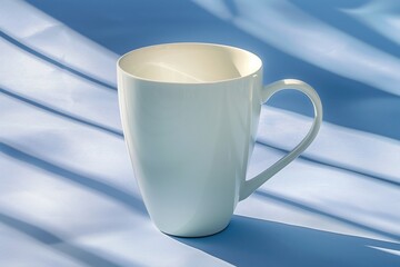Obraz premium White cup resting gracefully on soft blue fabric, illuminated by gentle sunlight in a calm morning setting