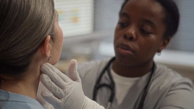 African American female physician in medical scrubs and gloves checking patient cervical lymph nodes and neck glands during clinical examination