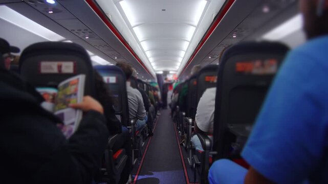 Rear aisle perspective inside airplane with passengers seated on both sides during mid flight evoking confinement shared presence monotony and calm order of commercial air travel