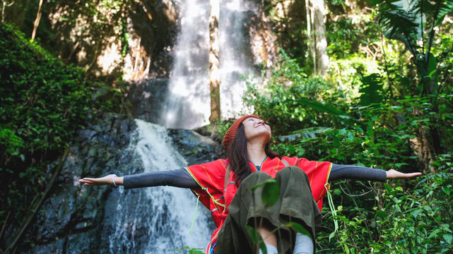 Portrait image of a woman with opened hands sitting in front of the waterfall in the forest