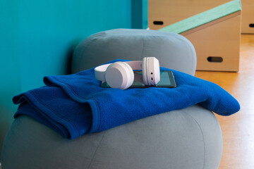 Blue fleece blanket draped over a gray pouf with white headphones and a tablet resting on top, against a teal wall in a modern interior setting © Irina Flamingo