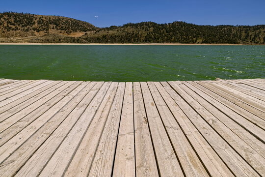 Wood boardwalk extending onto the emerald-green water of Lake Aguelmame Sidi Ali, the Middle Atlas mountains in background. Midelt prov.-Morocco-121