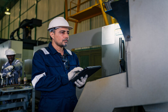 Factory man engineer using digital tablet worker operating CNC machine in manufacturing plant. Professional technician wearing uniform safety helmet maintenance production process heavy equipment
