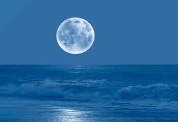 Night sky with blue moon in the clouds sea wave in the foreground 