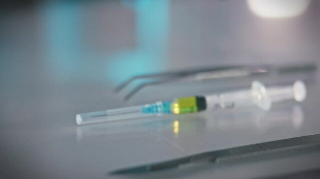 A medical professionals hands carefully grasp a prepared syringe containing medication amidst an array of surgical instruments, including a scalpel and tweezers, on a hospital operating room table