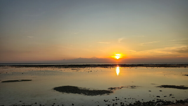 Golden sunlight descends as calm waters mirror soft clouds and sky