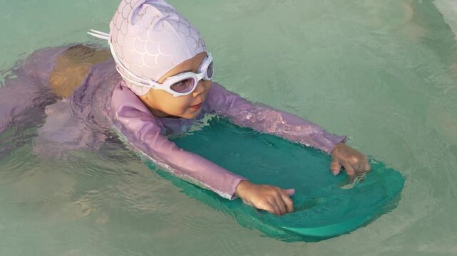 slow motion of preschool child girl learning to swim with board in swimming pool
