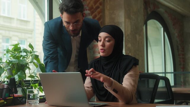 Arabian business team Muslim female using laptop man CEO coming checking work discussing internet task businesswoman in hijab working computer cyberspace talking with boss mentor together in office