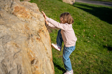 Little girl jumping on decorative stones in city park. Active spring play and outdoor childhood lifestyle.
