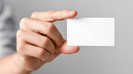 Obraz premium Hand holding blank white business card against a neutral gray background, showcasing space for text or design elements in a professional context