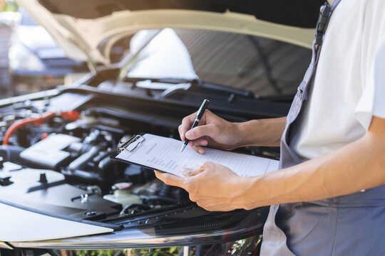 Auto check, car service shop concept. Automobile repairman writing job checklist on clipboard, mechanic checking engine to estimate repair machine, inspecting maintenance by engineer at vehicle garage