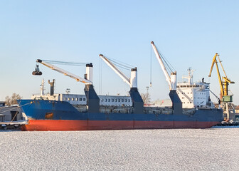 Blue cargo ship with cranes undergoing maintenance at a shipyard in Tallinn port, Estonia, during cold sunny winter season.