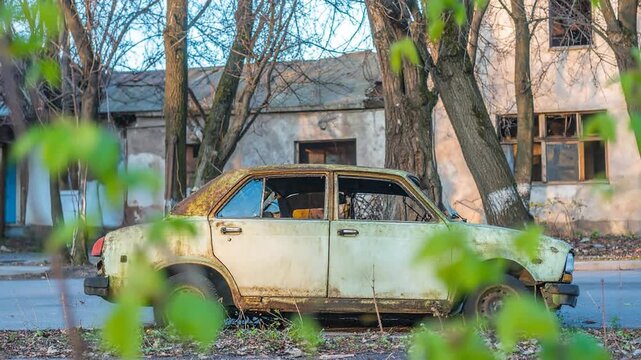 Abandoned vintage car with rusty body parked on the side of the road in front of an old building.