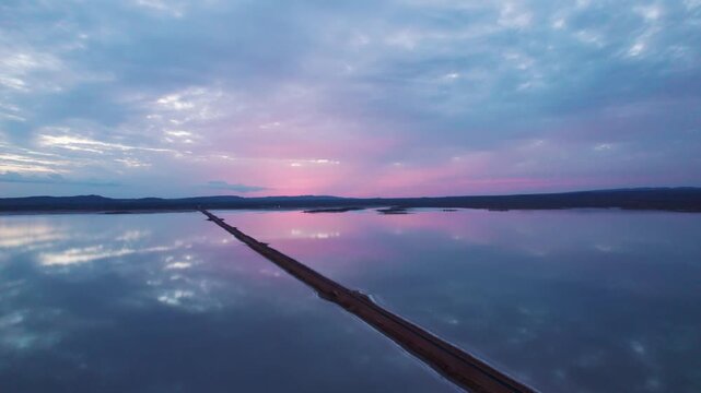 4K Aerial view of road to heaven after sunset, dark clouds in sky and reflection of clouds in water. Road passing through salt water lake in Great Rann of Kutch. Road connects Khavda and Dholavira vil