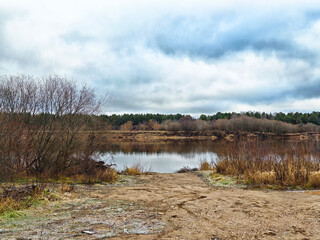 The serene landscape features a picturesque riverbank bathed in the warm glow of late afternoon light. Dark clouds drift lazily across the sky, casting gentle shadows on the tranquil scene