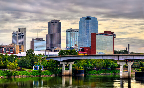 Little Rock skyline in Arkansas. Downtown city view features the Main Street Bridge with a yellow streetcar crossing the Arkansas River near Riverfront Park under a cloudy sky