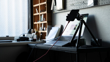 リモートワークのデスク風景 ノートパソコンと三脚に固定されたスマートフォン ライブ配信 / Remote work desk setup with laptop and smartphone on tripod, live streaming concept