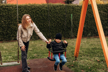 Obraz premium Woman happily pushes young boy on a bright yellow playground swing at a grassy park on an overcast afternoon