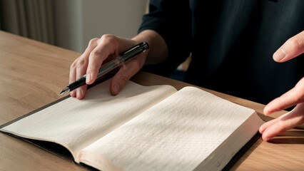 ノートに書き物をする男性の手元 思考の整理 ジャーナリング 丁寧な暮らし / Hands writing in notebook with pen and orange on table, journaling and planning concept