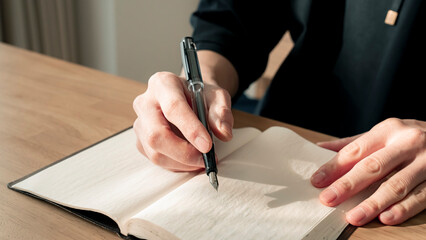 ノートに書き物をする男性の手元 思考の整理 ジャーナリング 丁寧な暮らし / Hands writing in notebook with pen and orange on table, journaling and planning concept