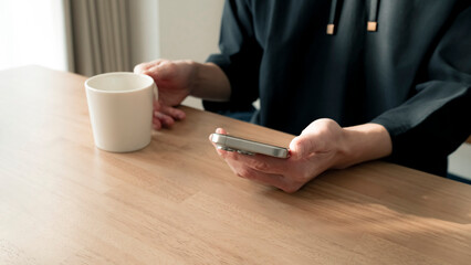 リラックスする男性の手元 スマートフォンとコーヒー ライフスタイル / Man using smartphone on wooden table, relaxed lifestyle