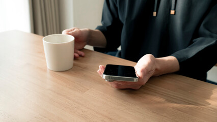 リラックスする男性の手元 スマートフォンとコーヒー ライフスタイル / Man using smartphone on wooden table, relaxed lifestyle