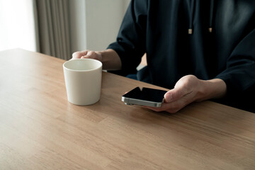 リラックスする男性の手元 スマートフォンとコーヒー ライフスタイル / Man using smartphone on wooden table, relaxed lifestyle