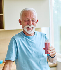 A senior man is eating healhty fruit breakfast and drinking juice and water in kitchen. Having a break after a morning exercise. The man is enjoying his meal, vitality, healthy eating and active senio