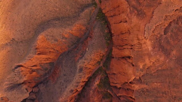 Overhead straight-down aerial drone flying forward over the vibrant red and orange sandstone clay landscape of Kok-Moynok 2 Canyon, Kyrgyzstan.