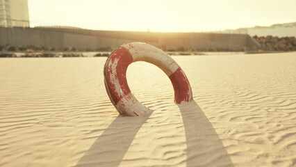 A weathered lifebuoy stands partially buried in golden sand as the sun sets on the horizon. © icetray