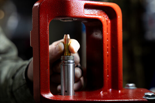 Close-up of a hand placing a bullet into a reloading press for ammunition manufacturing