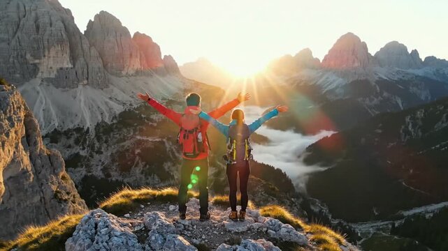 Hikers watch sunrise over mountains in Dolomites while standing on rocky ledge