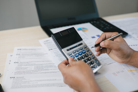Close up of professional calculating income tax with calculator and documents on desk. Concept of tax preparation, financial planning, accounting services and regulatory compliance.