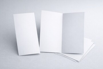 Fototapeta premium A stack of unfolded and folded blank white brochures sits ready for branding mockups on a light gray surface.