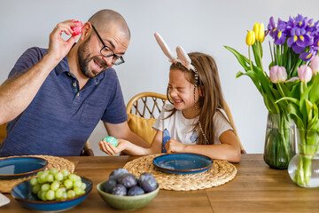 Father and daughter playing tapping game with colorful easter eggs at a festive dining table...