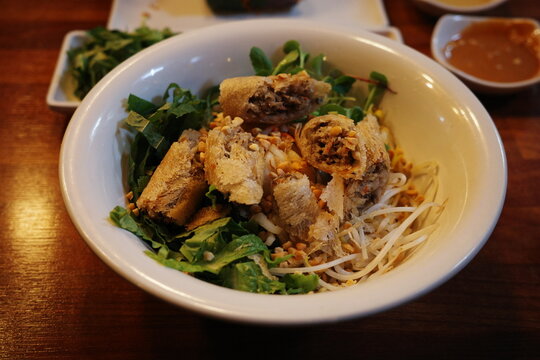 Vietnamese bun thit nuong rice vermicelli bowl with grilled pork, herbs, pickled vegetables, and crunchy topping. Traditional street food served on wooden table with dipping sauce.